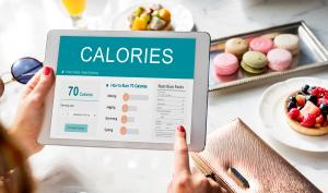 планшет у жіночих руках з написом CALORIES (калорії) латиницею на тлі висококалорійних продуктів харчування