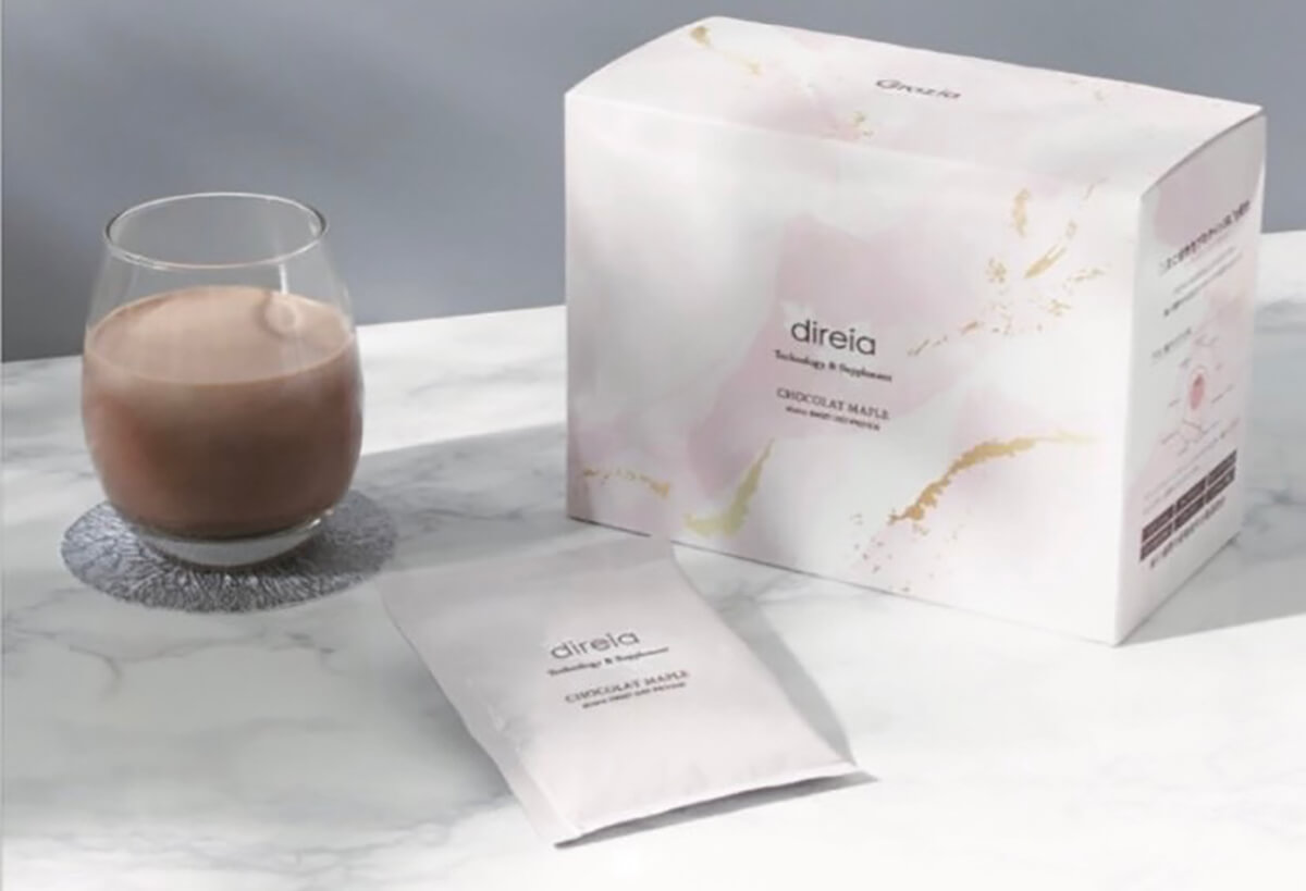 Коробка і саше DIREIA Sweet Diet PROTEIN і приготований напій у прозорій скляній склянці на столі