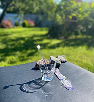 Іонна зубна щітка APAGARD 'Crystal' Toothbrush у прозорій скляній склянці на чорному тлі в літньому саду