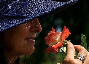 Жінка зрілого віку в капелюсі нюхає квітку троянди