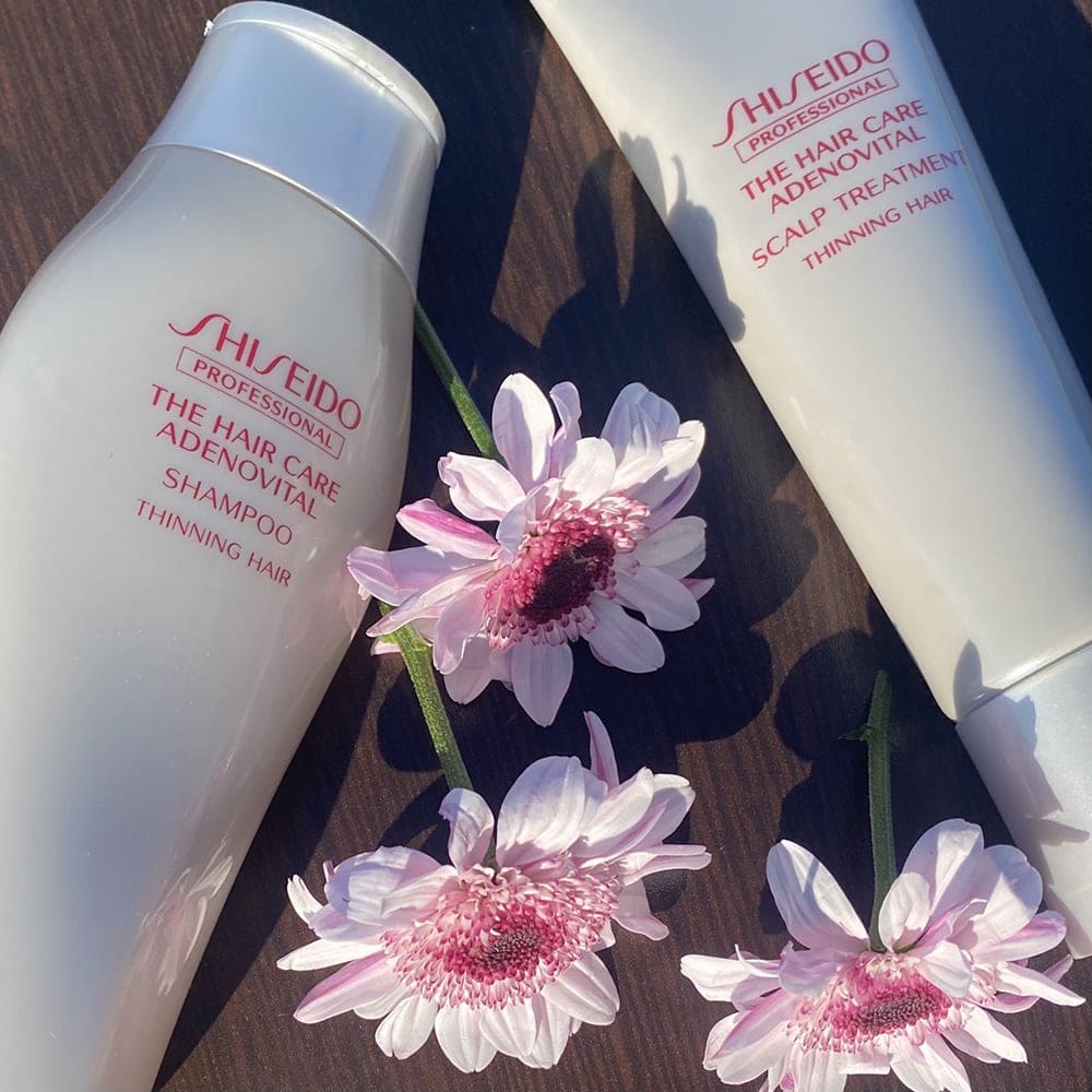 Шампунь і бальзам для шкіри голови SHISEIDO ADENOVITAL на темно-коричневій дерев'яній поверхні з фіолетовими квітами