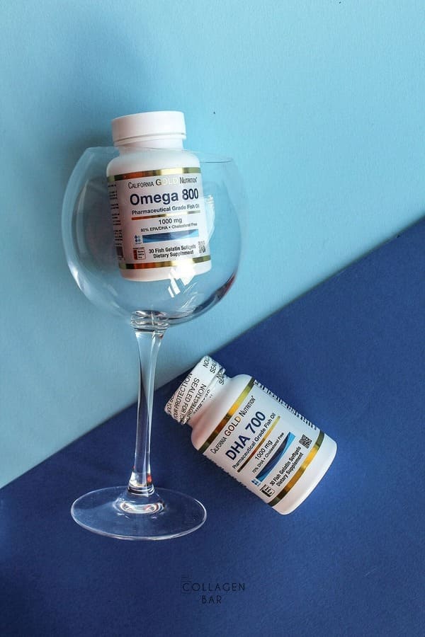 Банки з Omega-800 та DHA-700 від California Gold Nutrition зі скляним келихом.