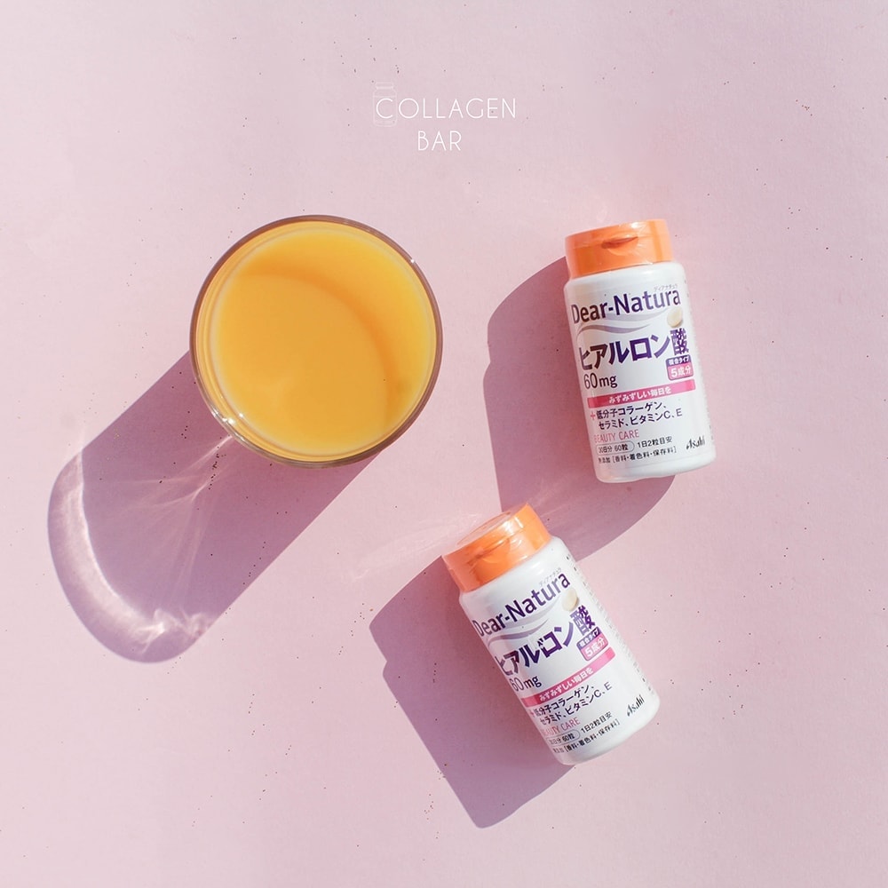 Две баночки гиалуроновой кислоты Dear-Natura и стакан апельсинового сока на розовом фоне. Вид сверху.