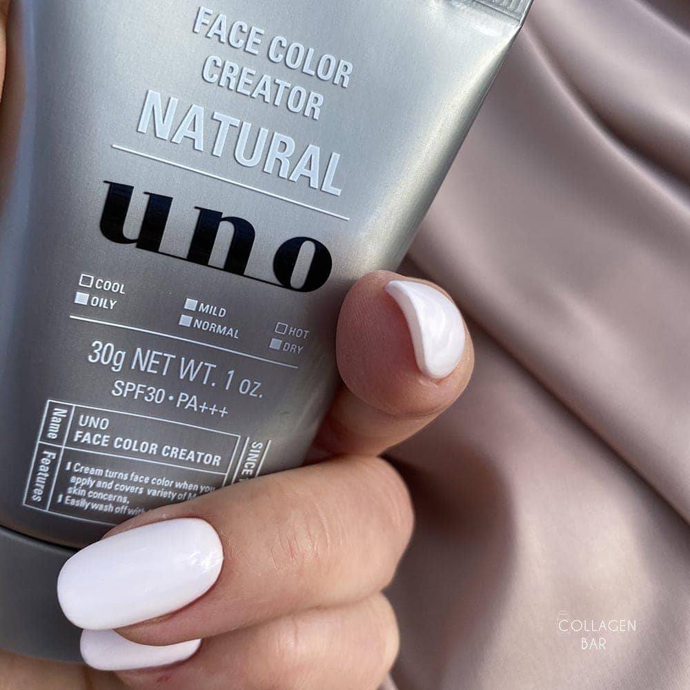 BB-крем SHISEIDO UNO Face Color Creator у жіночій руці з манікюром білого кольору на тлі коричневої тканини