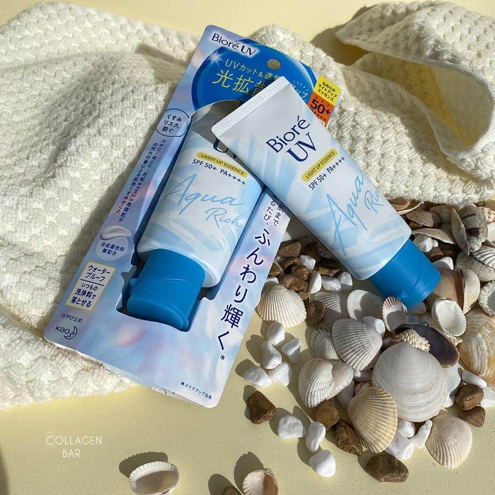 Два санскріни Biore UV Light UP Essence на білому рушнику з морськими мушлями