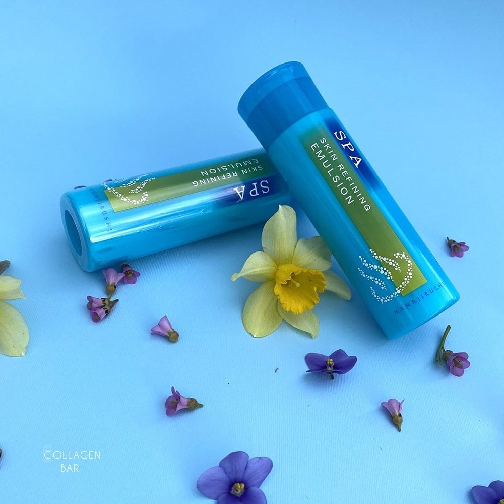 Два флакона эмульсия Hanajirushi SPA Skin Refining Emulsion на голубом фоне с цветами нарцисса и фиолетовой фиалки