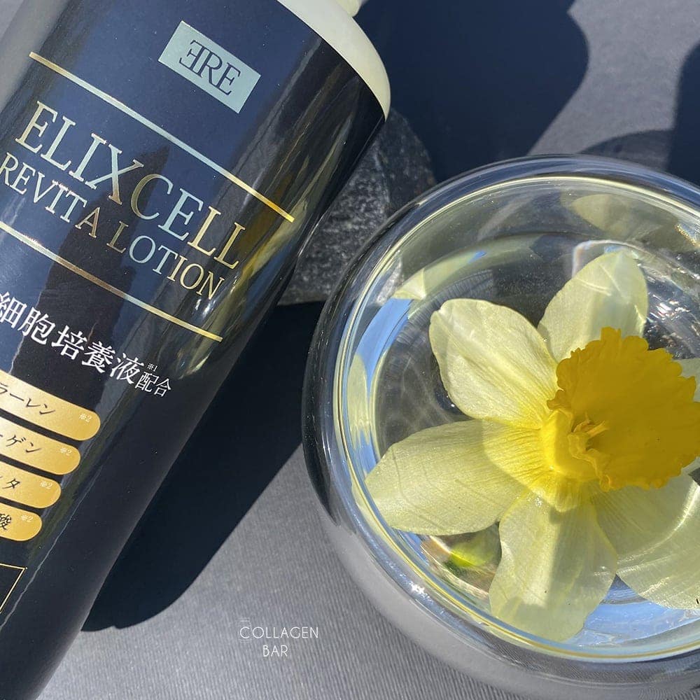 Фрагмент флакона с Elixcell Revita Lotion с прозрачной стеклянной вазочкой с нарциссом на черном фоне