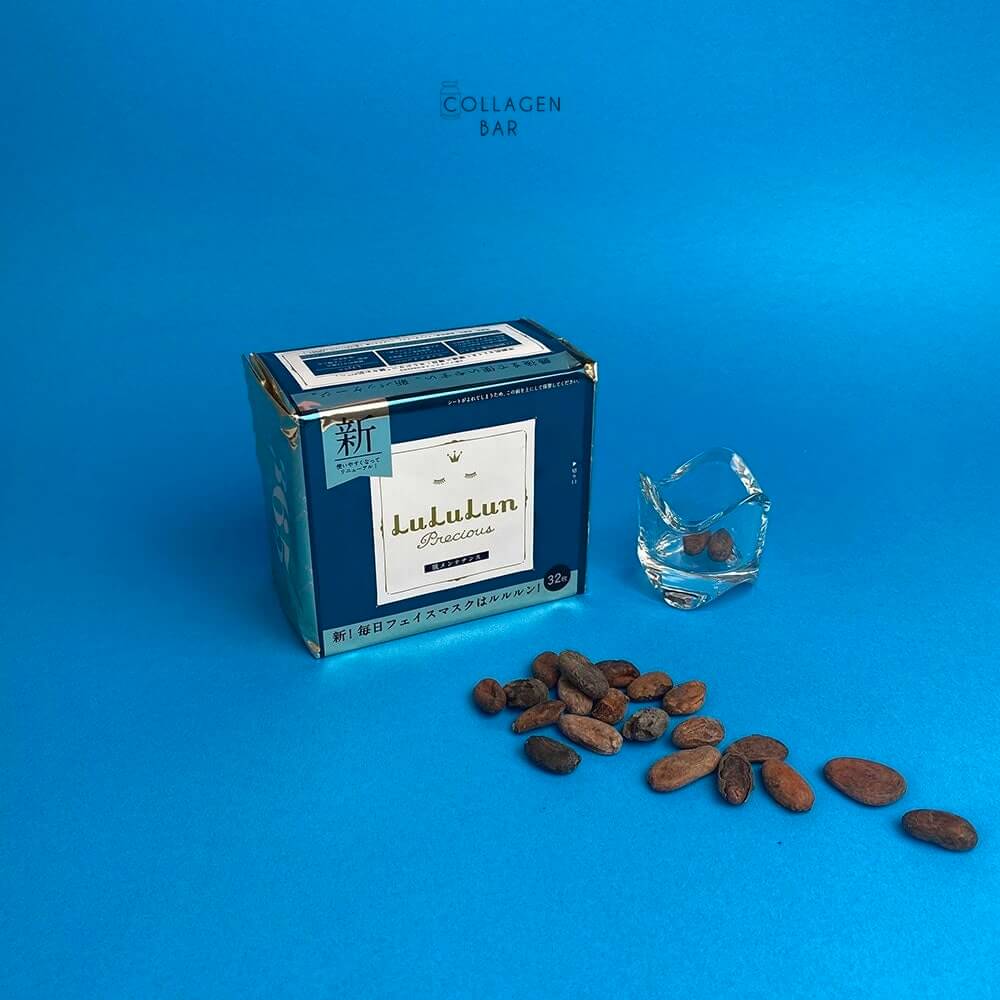 Маска LuLuLun Precious GREEN в упаковці на 32 штуки, какао-боби і прозорий підсвічник на синьому фоні