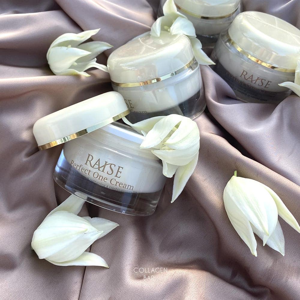 Три баночки крему RAISE Perfect One Cream на світло-коричневій тканині з білими квітками