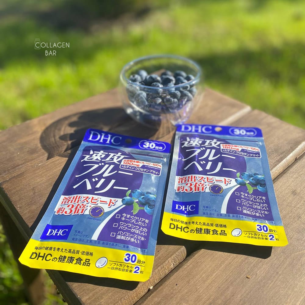 Дві упаковки комплексу на основі екстракту чорниці &ldquo;Haste Blueberry&rdquo; від DHC з ягодами чорниці в скляній піалі на дерев'яному столику в літньому саду