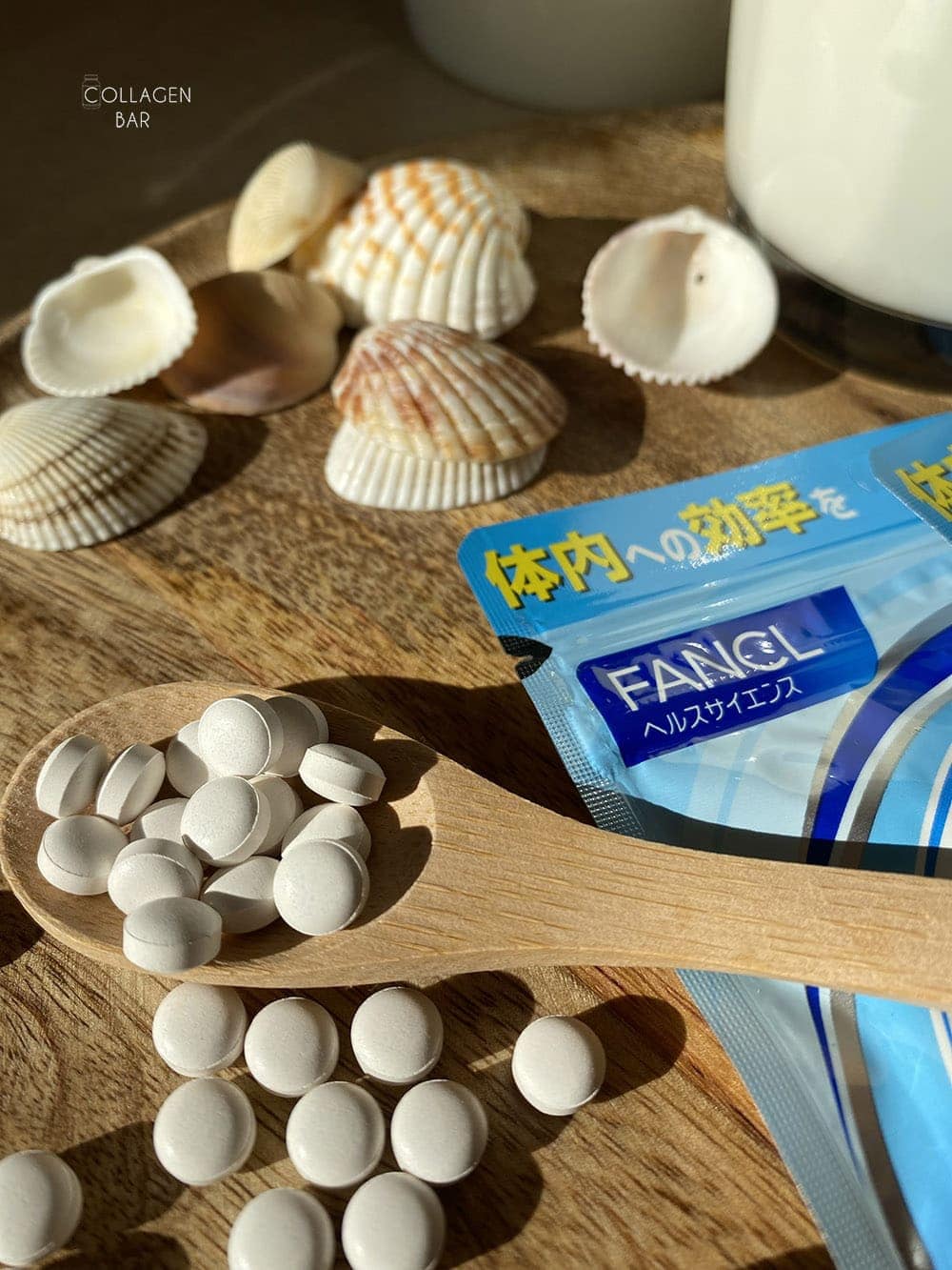 Фрагмент упаковки комплексу кальцій (Ca) + магній (Mg) FANCL з морськими раковинами на дерев'яній тарілці з дерев'яною ложкою, в якій знаходяться білі таблетки з упаковки