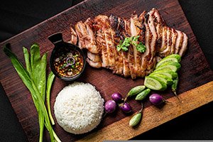 Жареное мясо, рис, овощи и приправы на деревянной сервировочной доске.