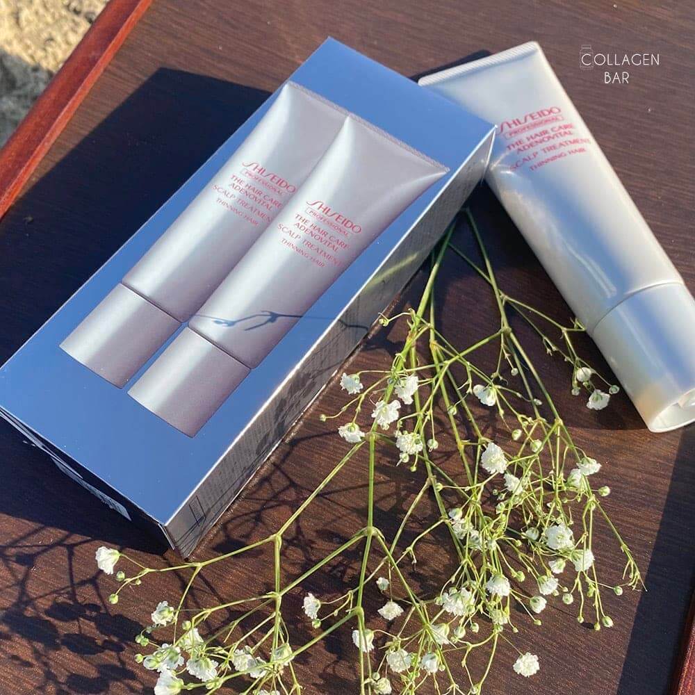 Бальзам для кожи головы SHISEIDO ADENOVITAL на темно-коричневой деревянной поверхности с веткой белых мелких цветов