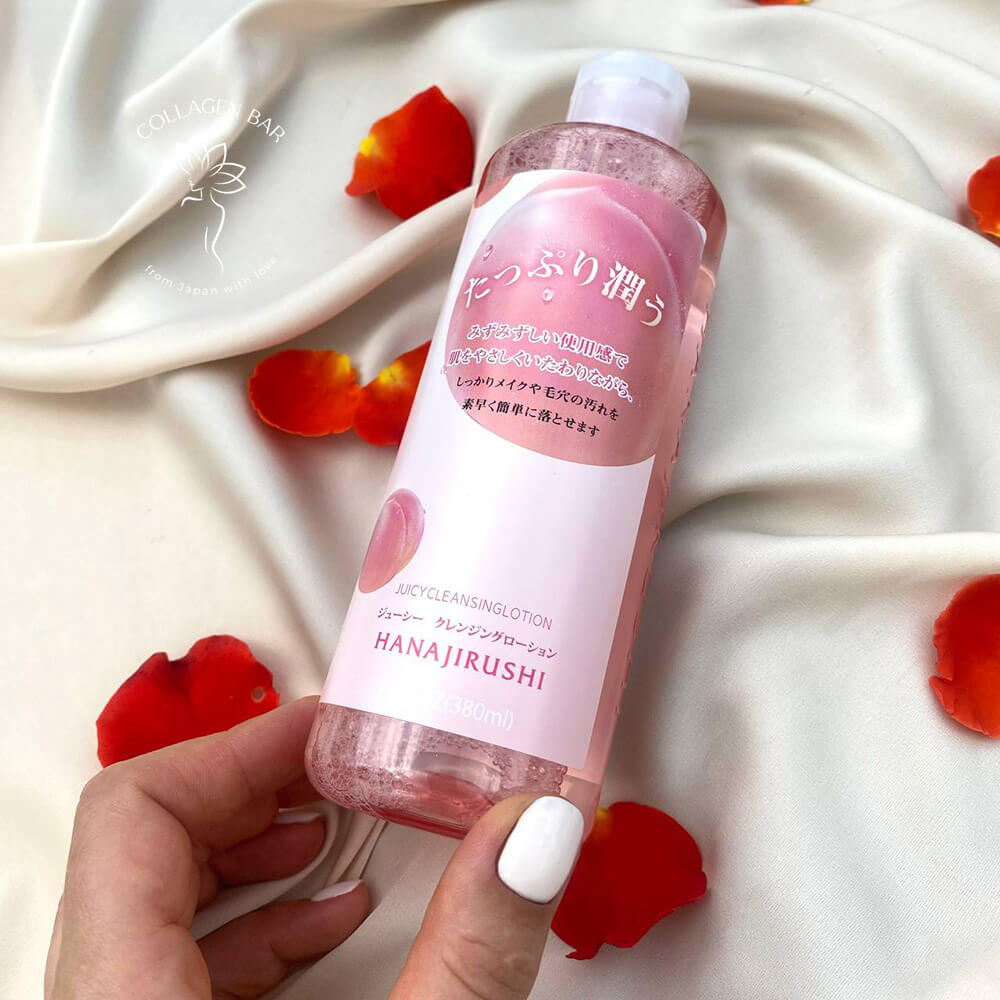 Лосьйон для демакіяжу та вмивання HANAJIRUSHI Juicy Cleansing Lotion у жіночій руці над світло-коричневою тканиною з пелюстками троянд