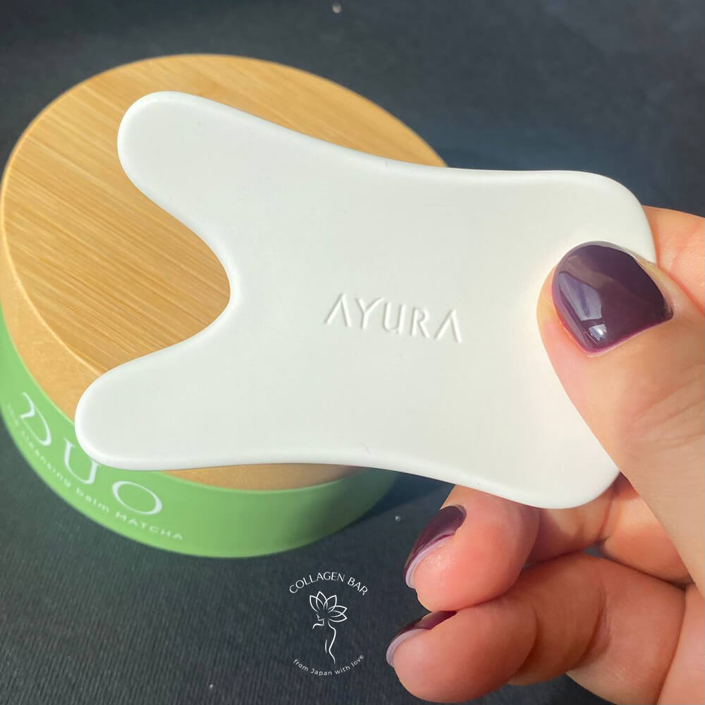 Плитка для массажа Гуаша AYURA Bicassa Plate Premium в женской руке с маникюром цвета бордо