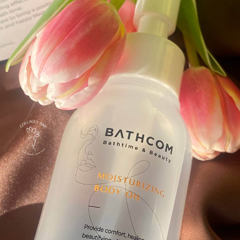 Фрагмент флакона BATHCOM Moisturizing Body Oil крупним планом з рожевими тюльпанами