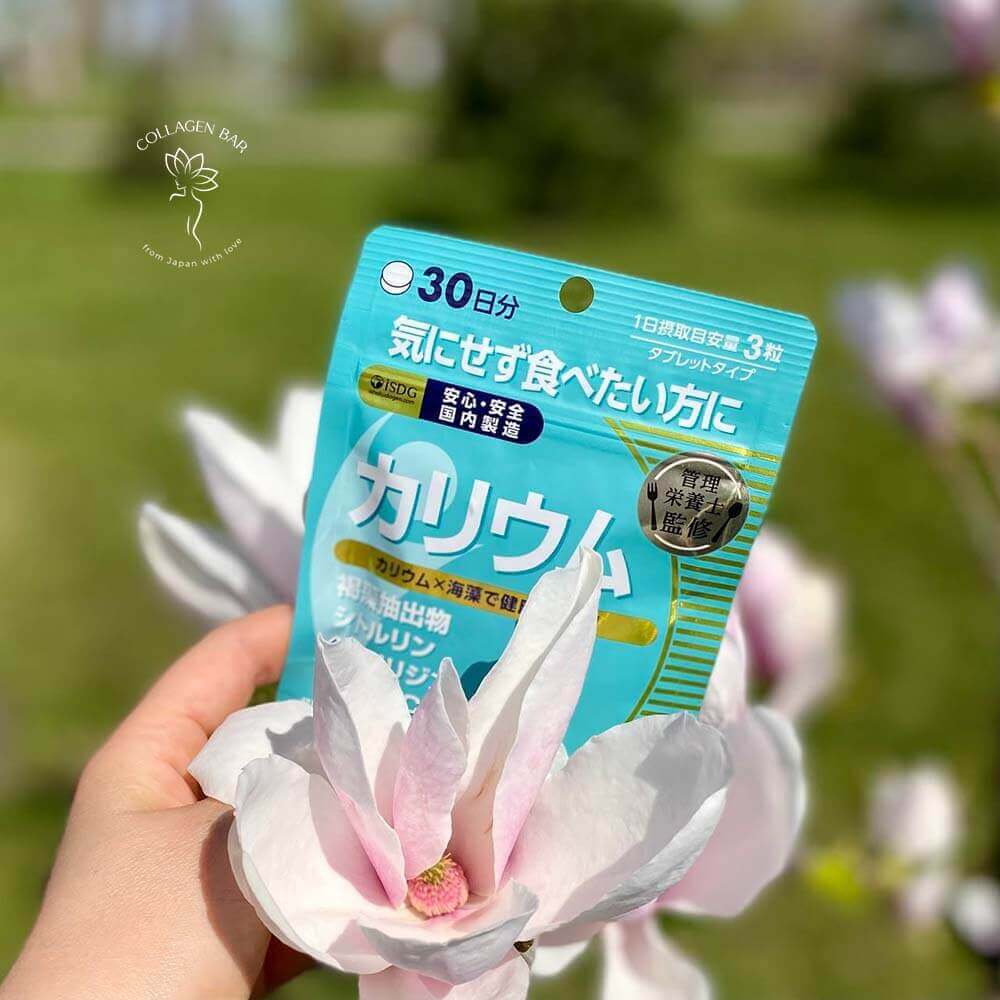 Упаковка ISDG Potassium Supplement у жіночій руці на тлі квітучих гілок магнолії у весняному саду