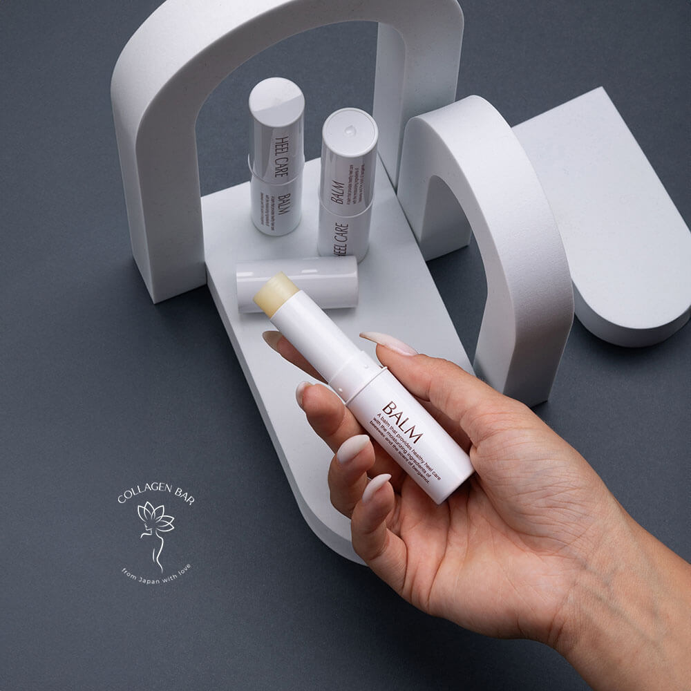 Открытый бальзам-стик для пяток MEIDAI Heel Care Balm в женской руке на фоне интсаляции с геометрическими фигурами