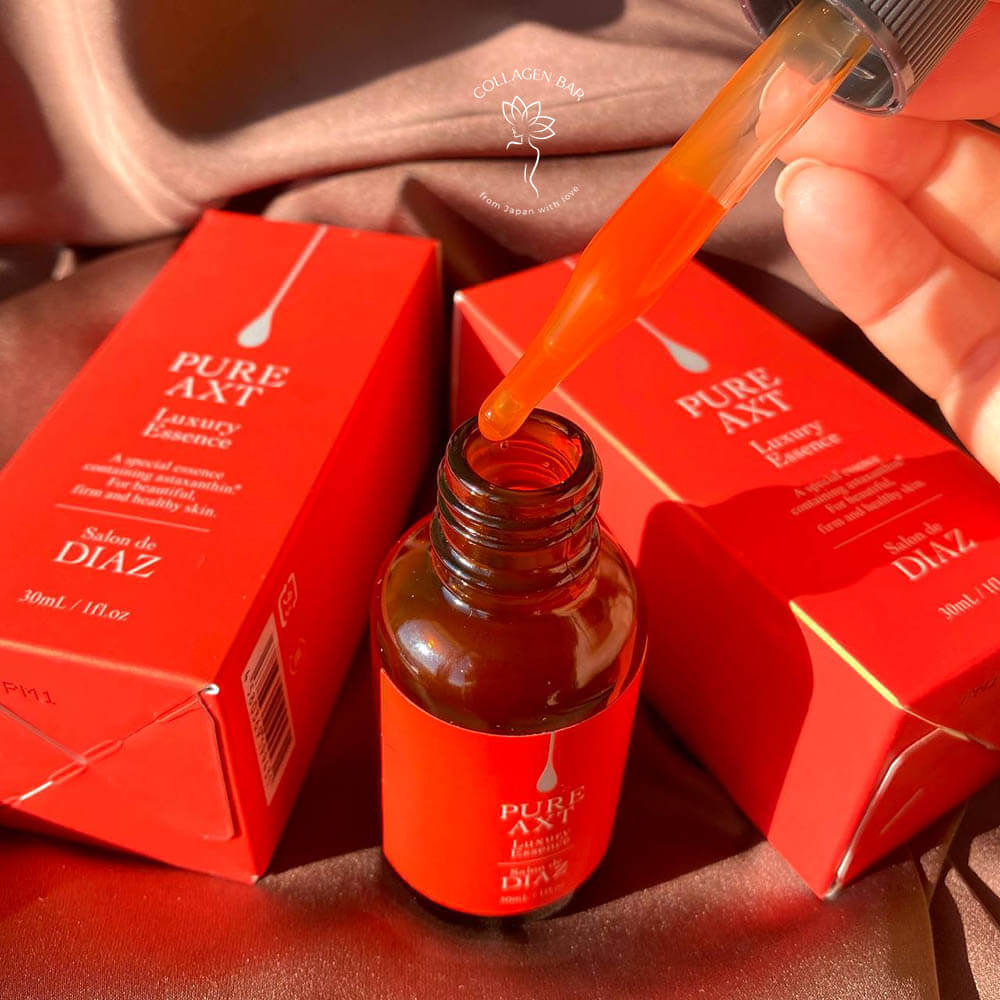 Піпетка з відкритого флакона сироватки SALON DE DIAZ Pure AXT Luxury Essence з яскраво-помаранчевим вмістом у жіночій руці
