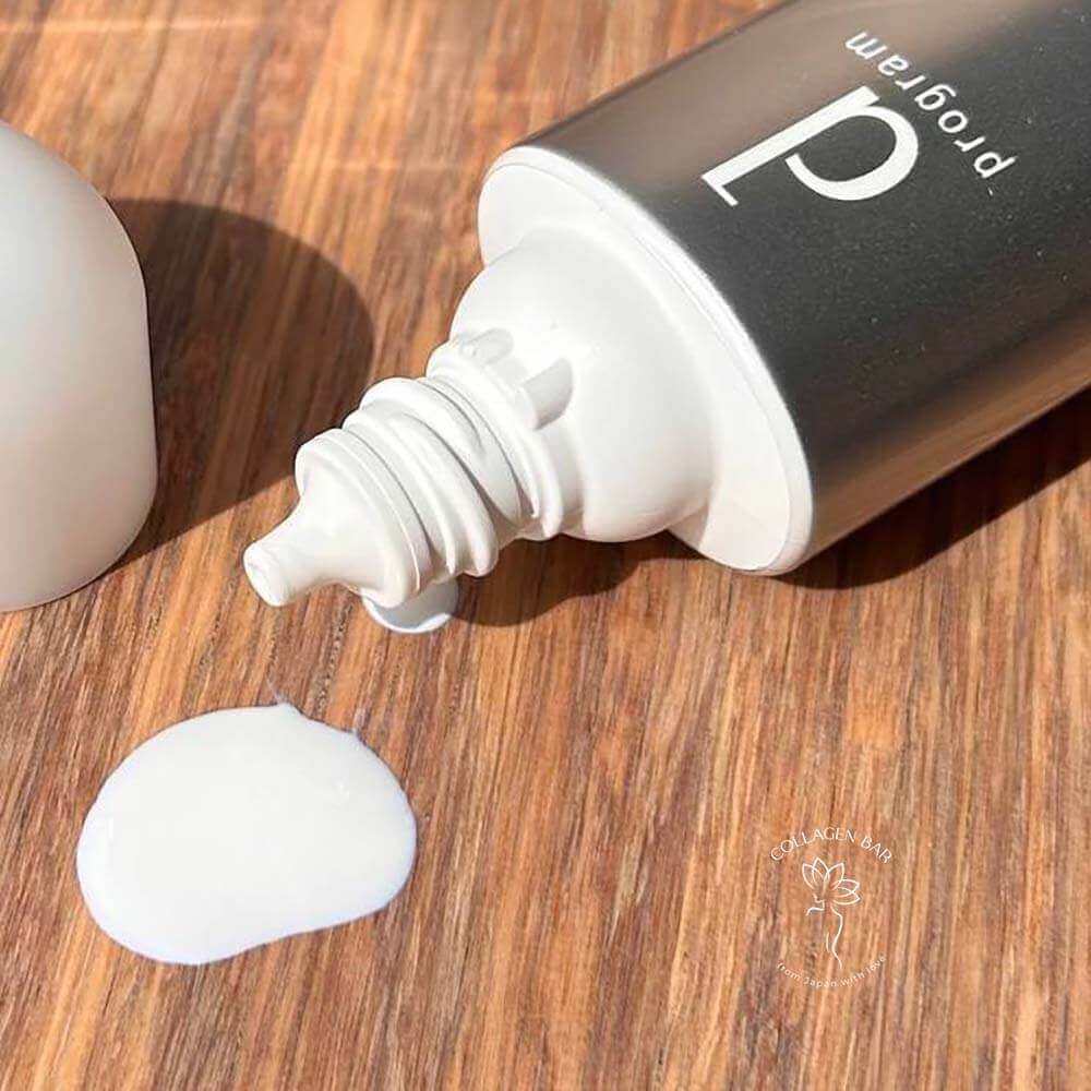 Відкритий тюбик SHISEIDO d Program Allergy Barrier Essence N з якого видавлено невелику кількість білої есенції на дерев'яний стіл. Великий план.