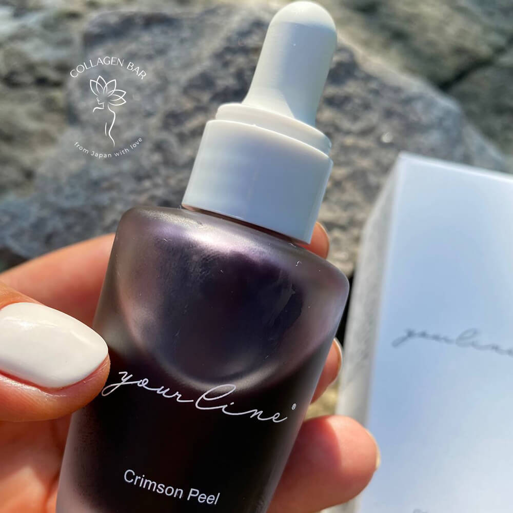 Багряний кислотний пілінг YOURLINE Crimson Peel у жіночій руці з білим манікюром над каменем